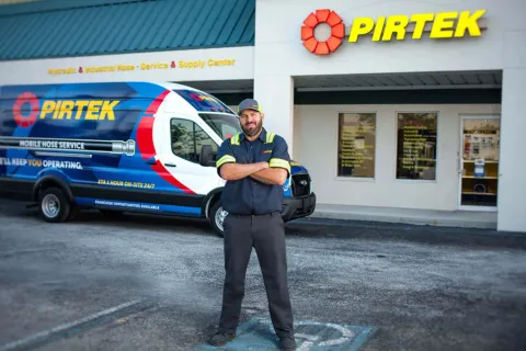 Pirtek technician stands with arms crossed in front of branded service van and store with PIRTEK signage.