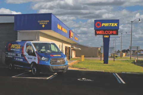 Pirtek service van parked outside customer service building with Pirtek welcome sign under blue sky with clouds