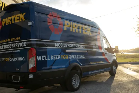 Blue Pirtek mobile hose service van parked outside during sunset with company branding and service details.