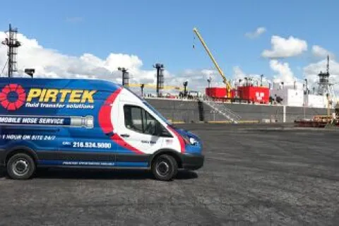 Blue and white PIRTEK mobile hose service van parked near industrial port with ship and crane in the background
