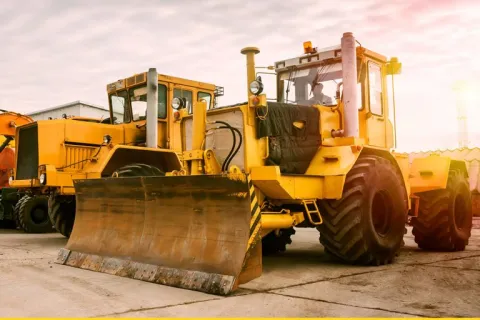Yellow bulldozers parked on concrete ground under a cloudy sky during sunset at a construction site.