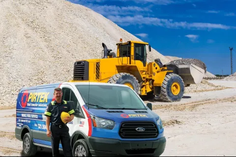 PIRTEK service van and worker with helmet in front of yellow loader at gravel site under blue sky