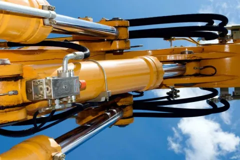 Close-up of yellow hydraulic machinery cylinders and pistons against a clear blue sky with clouds.