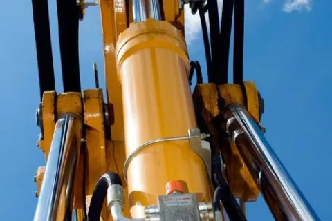 Close-up of yellow hydraulic machinery cylinders and pistons against a clear blue sky with clouds.