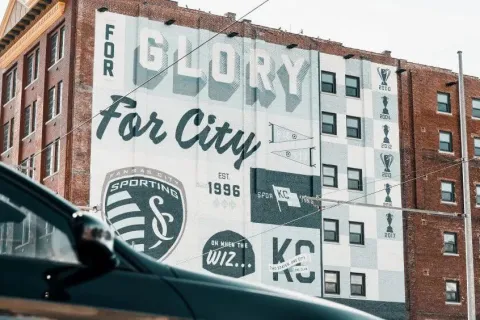 Sporting Kansas City mural on brick building celebrating soccer achievements and city pride with trophies and logos.