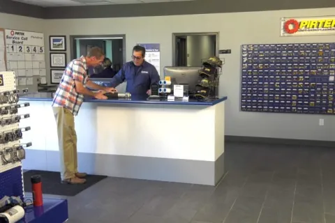 Customer at service counter assisted by store employee in a hydraulic parts and service shop interior.