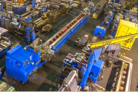 A large industrial workshop with blue machinery, yellow crane, and organized metalworking equipment.