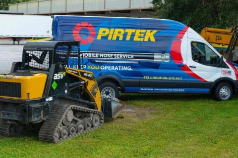 Pirtek mobile hose service van parked on grass next to a yellow ASV RT-50 compact track loader.