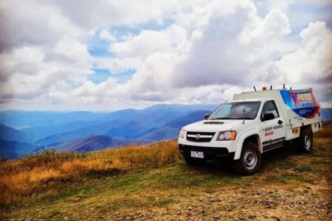 White utility truck parked on grassy hilltop with mountains and cloudy sky in the background