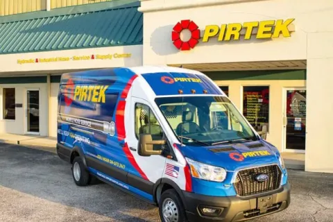 Blue and white PIRTEK service van parked outside a PIRTEK service and supply center building with company signage.