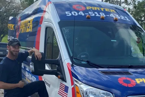 Service van with PIRTEK logo and phone number 504-518-4321 parked outdoors with a smiling worker beside it