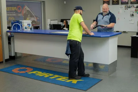 Customer and employee interacting at a service counter with Pirtek logo mat on the floor