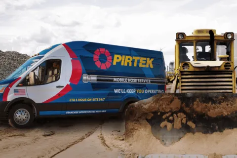 Pirtek mobile hose service van parked next to a bulldozer in a sandy construction site under cloudy sky.