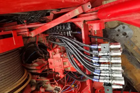 Close-up of hydraulic system with multiple hoses and metal fittings on industrial red machinery.