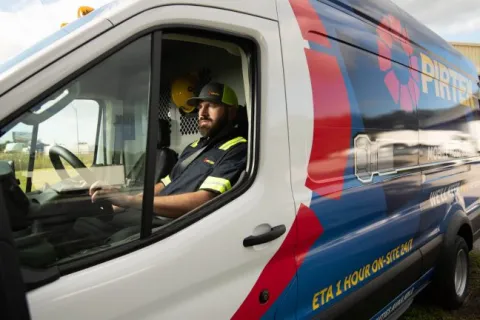 Man in uniform sitting inside a branded service van parked outdoors near a building.