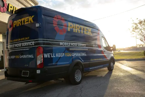 Blue PIRTEK mobile hose service van parked outside at sunset with company branding and slogan visible.