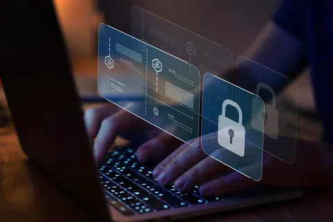 Hands typing on laptop keyboard with digital security icons and data interface overlays in dark environment