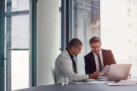 Two businessmen collaborating over documents and laptop in a bright modern office with large windows