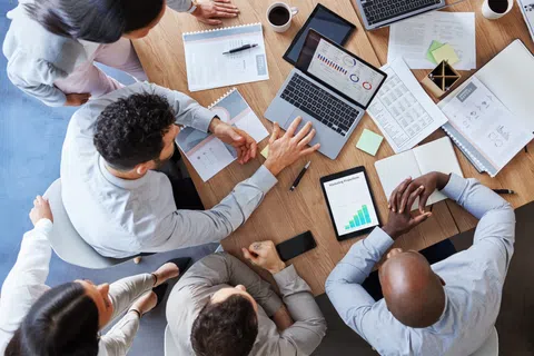 Business team collaborating over data charts and laptops in a meeting around a wooden table.