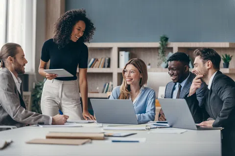 Diverse business team collaborating around a table with laptops and documents in a modern office setting.