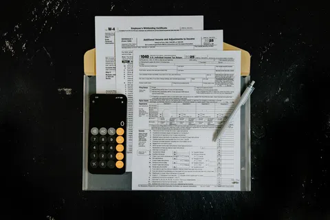 Tax forms including W-4 and 1040 with a calculator and pen on a black surface folder.