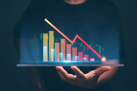 Person holding a tablet displaying a declining bar and line graph symbolizing financial loss or market downturn.