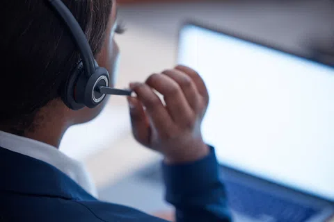 Customer service representative wearing headset working on laptop with blank screen in office.