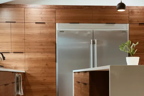 Modern kitchen with wooden cabinets, stainless steel refrigerator, island with white countertop, and hanging lights.