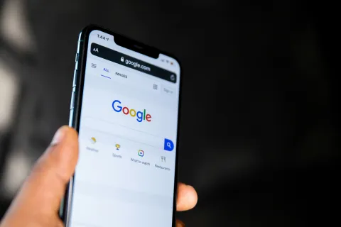 Hand holding smartphone displaying Google search homepage with search bar and icons on screen.