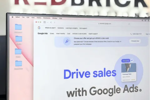 Computer screen displaying Google Ads website with RedBrick logo blurred in the background.