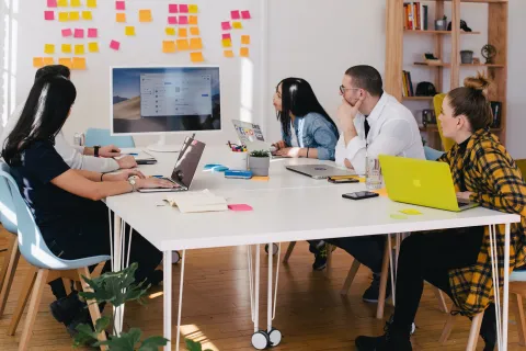 a group of people sitting around a table with laptops