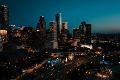 Nighttime cityscape of a modern urban skyline with illuminated skyscrapers and busy highways in Houston.