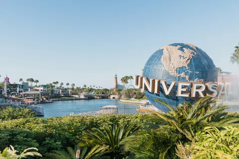 Universal Studios globe sculpture with water and greenery under clear blue sky at theme park entrance.