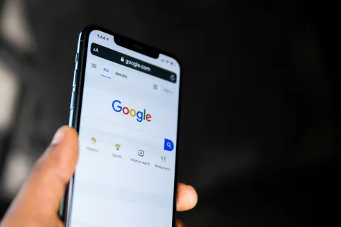 Person holding smartphone displaying Google search home page with visible search options and logo.