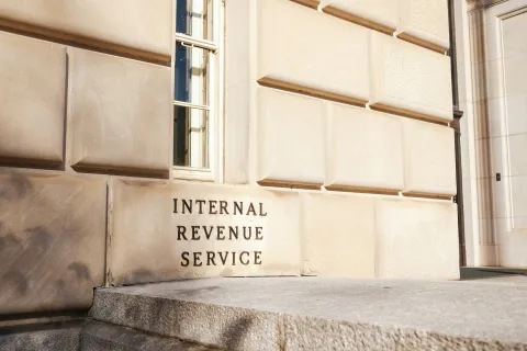 Stone building entrance with Internal Revenue Service sign engraved on beige wall under window.