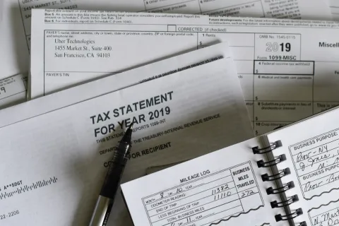 Tax documents, 2019 tax statement, mileage log, and pen arranged on a desk for tax filing preparation.