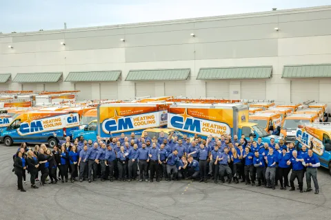 Group photo of CM Heating and Cooling employees standing in front of company service vans with branded logos.