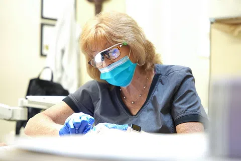 Female medical professional wearing mask and gloves focused on patient care in a bright clinical setting.