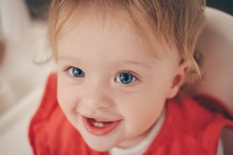Close-up of a smiling toddler with bright blue eyes wearing a red outfit in soft lighting