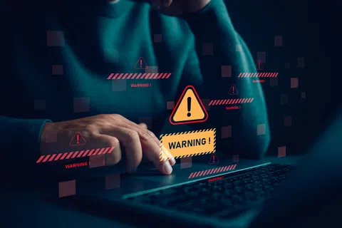 Person using laptop with multiple digital warning alerts and caution symbols floating above the keyboard.