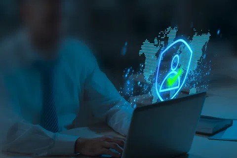 Businessman working on laptop with digital security shield and user icon hologram glowing in office at night