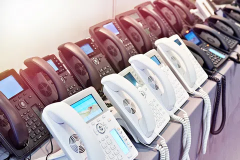 Rows of black and white office desk phones with digital screens arranged on a table.