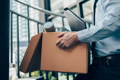 Man in business attire holding an open cardboard box with office items inside near a modern stairwell.