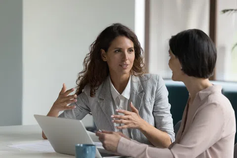 Two professional women engaged in a business discussion with a laptop and documents on the table