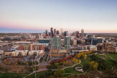 Aerial view of a city skyline at dusk with mixed urban buildings and a green park in the foreground.