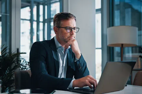 Focused businessman working on laptop in modern office with large windows and natural light