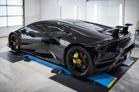Sleek black sports car with yellow brake calipers on a hydraulic lift in a bright garage setting.