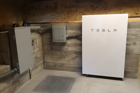 Tesla Powerwall home battery system installed on concrete basement wall with electrical panels