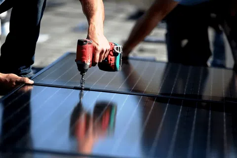 Worker using a drill to install solar panels on a rooftop under sunny conditions