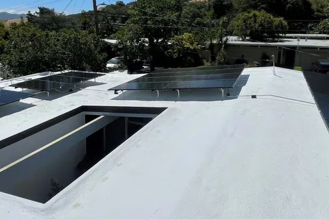 Solar panels installed on a white flat rooftop with trees and mountains in the background on a sunny day